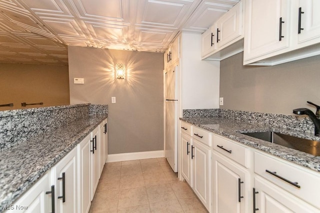 kitchen with an ornate ceiling, stone countertops, white cabinetry, a sink, and baseboards