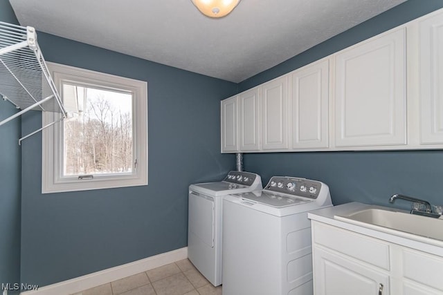 washroom with cabinet space, baseboards, separate washer and dryer, a sink, and light tile patterned flooring