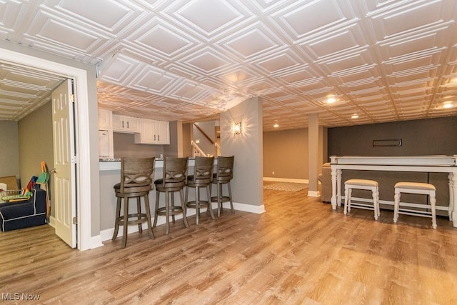 kitchen featuring a kitchen breakfast bar, baseboards, white cabinets, light wood-type flooring, and an ornate ceiling