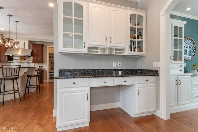 kitchen featuring light wood-style floors, ornamental molding, under cabinet range hood, white cabinetry, and built in desk