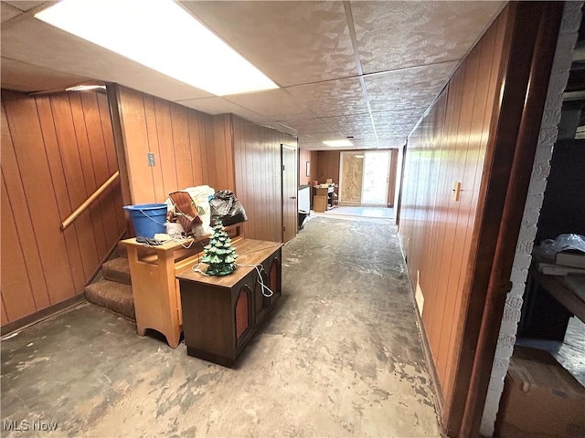 hallway featuring stairs, concrete floors, and wooden walls