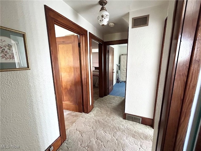 hall featuring carpet, visible vents, and a textured wall