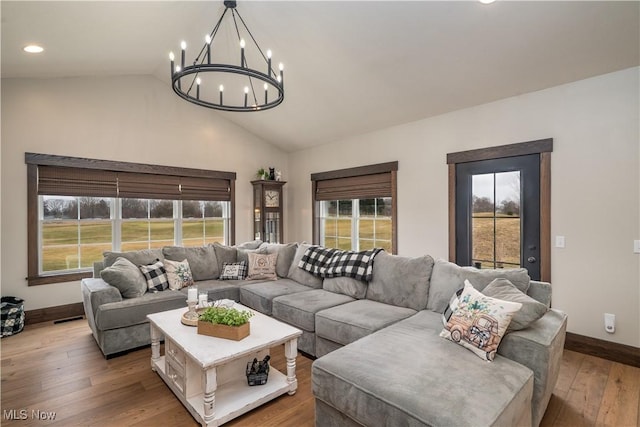 living room featuring a notable chandelier, wood-type flooring, visible vents, vaulted ceiling, and baseboards