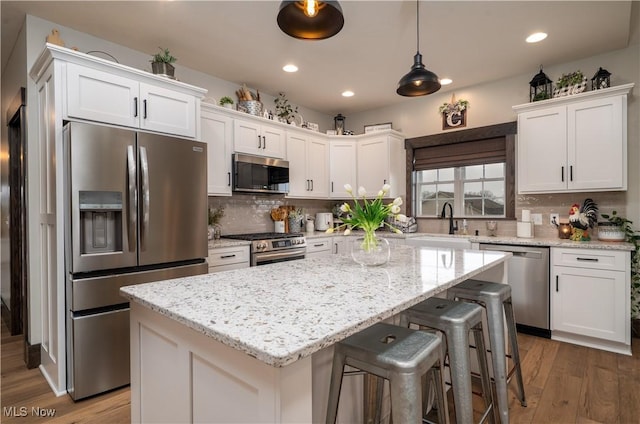 kitchen featuring tasteful backsplash, white cabinets, a kitchen island, wood finished floors, and stainless steel appliances