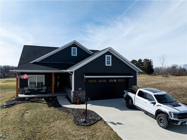 view of front of property with a porch, an attached garage, driveway, stone siding, and a front yard