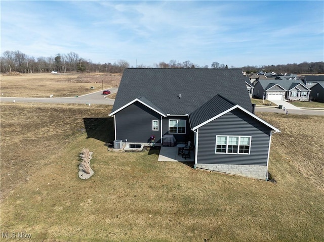 rear view of property with a yard, roof with shingles, and a patio area