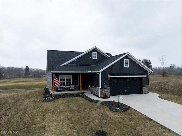 view of front of home with covered porch, stone siding, a front lawn, and driveway