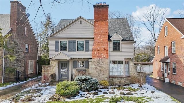 view of front of home with stone siding, a shingled roof, a chimney, and driveway