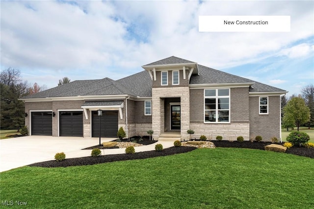 prairie-style home with driveway, stone siding, roof with shingles, an attached garage, and a front lawn