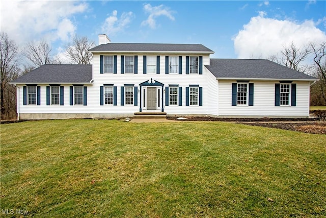 colonial inspired home featuring roof with shingles, a chimney, and a front yard