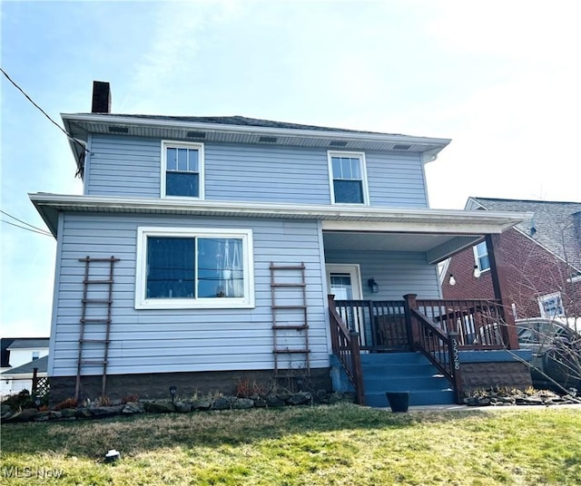 back of house with covered porch, a chimney, and a lawn