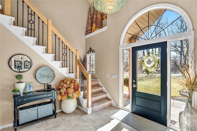 foyer with a healthy amount of sunlight, stairs, a towering ceiling, and a chandelier