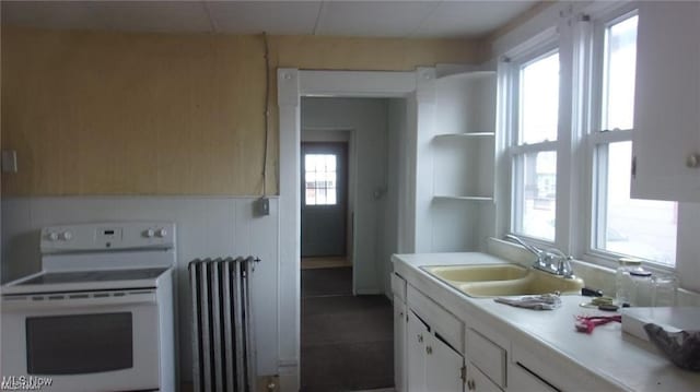 kitchen with a sink, white cabinetry, light countertops, white range with electric stovetop, and radiator heating unit