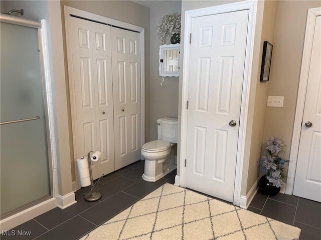 full bath featuring toilet, tile patterned flooring, baseboards, and a shower stall