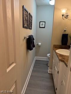 half bathroom featuring wood finished floors, vanity, toilet, and baseboards