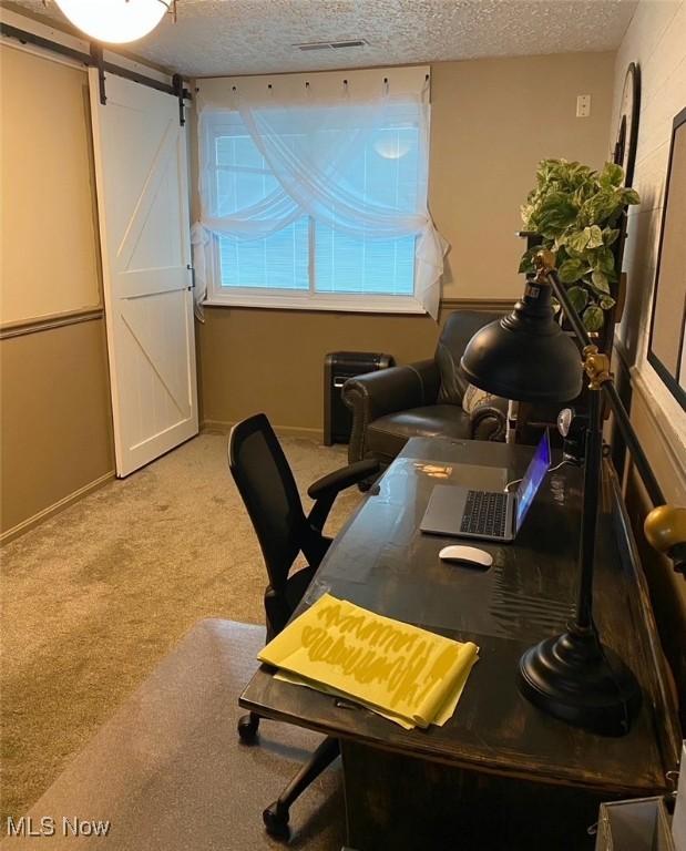 carpeted office with a barn door, baseboards, and a textured ceiling