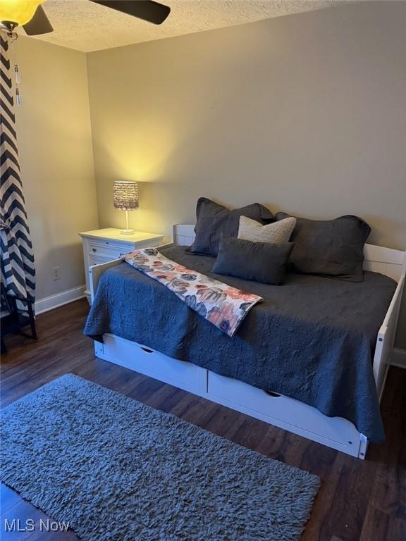 bedroom featuring ceiling fan, a textured ceiling, baseboards, and wood finished floors