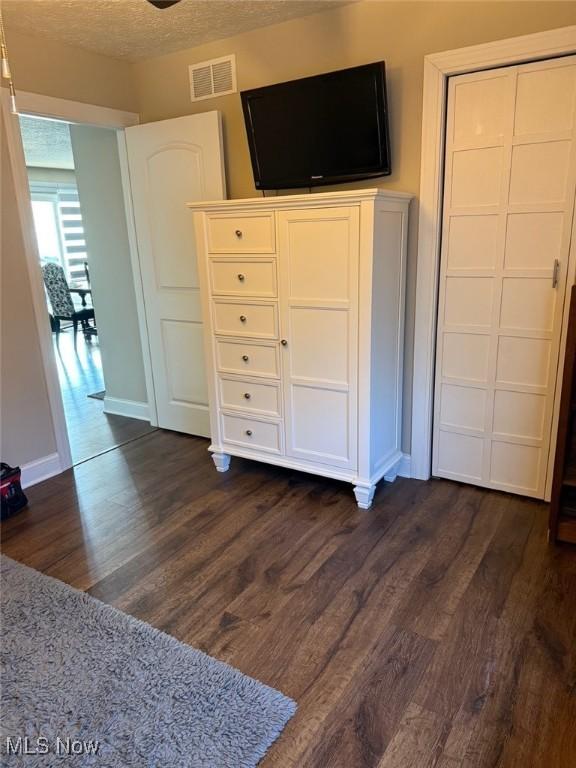 unfurnished bedroom with visible vents, dark wood finished floors, a textured ceiling, and baseboards