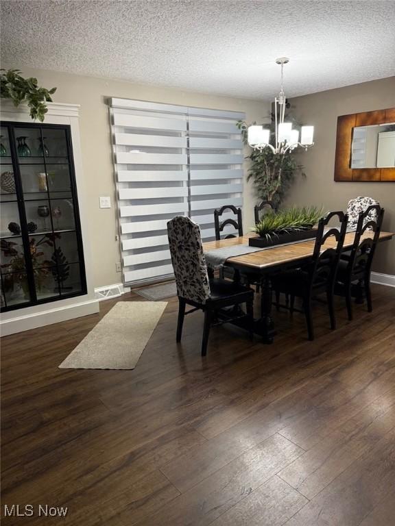 dining room with a textured ceiling, wood-type flooring, baseboards, and a notable chandelier