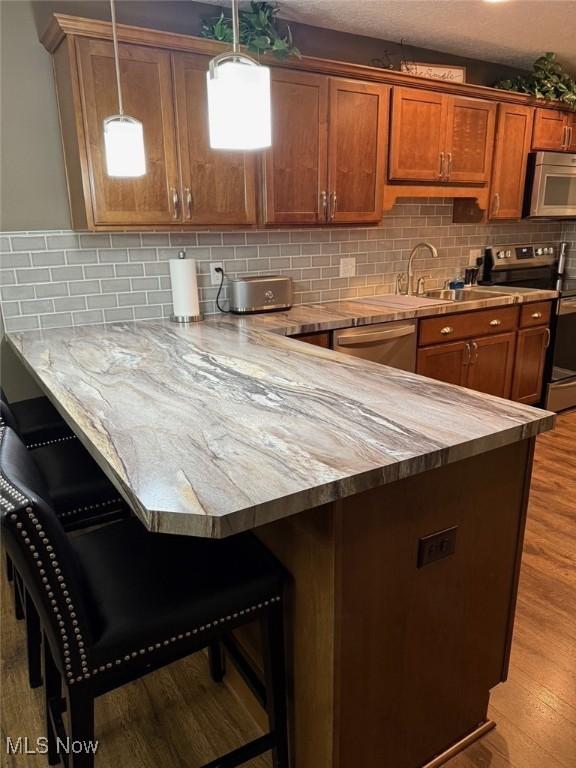 kitchen featuring brown cabinetry, appliances with stainless steel finishes, a kitchen breakfast bar, light wood-type flooring, and a sink