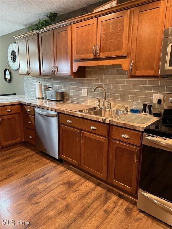 kitchen featuring stainless steel appliances, dark wood finished floors, a sink, and backsplash