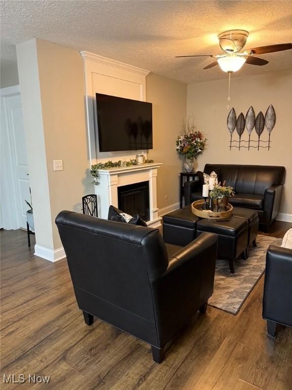 living area featuring a textured ceiling, a fireplace, dark wood finished floors, and baseboards