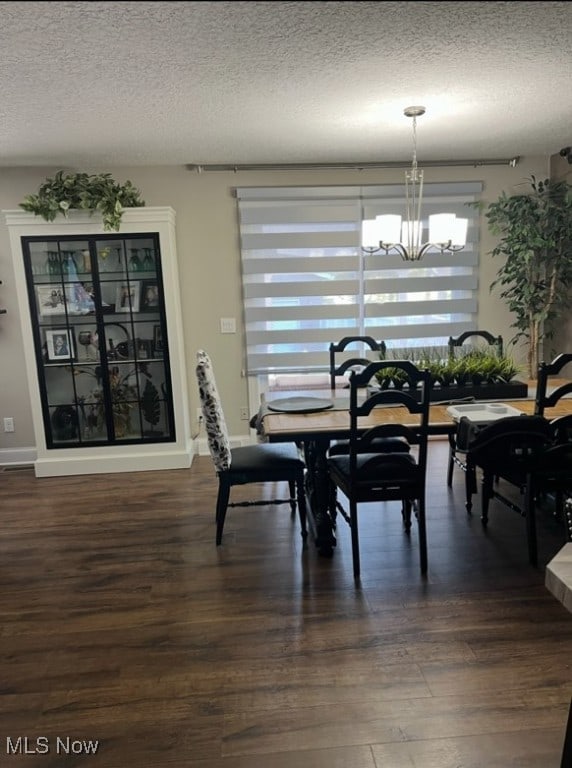 dining room featuring a textured ceiling, dark wood-style flooring, baseboards, and an inviting chandelier