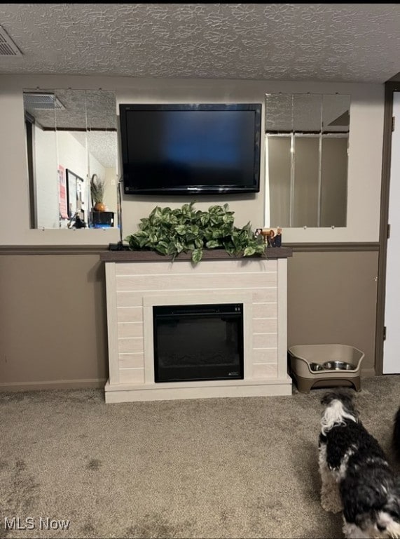 unfurnished living room with a glass covered fireplace, visible vents, a textured ceiling, and carpet