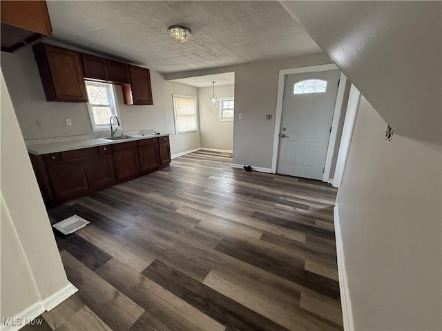 kitchen featuring a textured ceiling, dark wood-type flooring, a sink, baseboards, and light countertops