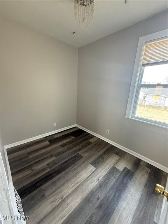 spare room featuring dark wood-type flooring and baseboards