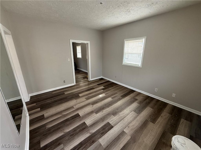 empty room featuring dark wood-style floors, a textured ceiling, a wealth of natural light, and baseboards