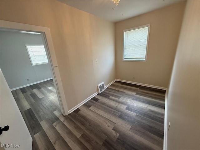 spare room with dark wood finished floors, visible vents, and baseboards