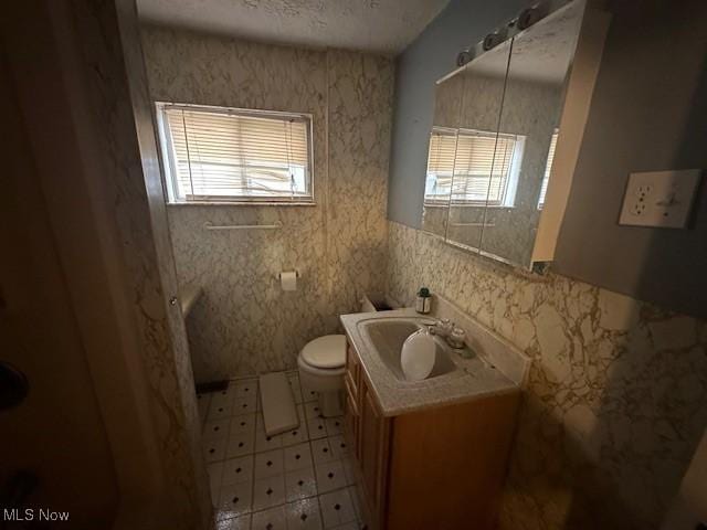 bathroom with a textured ceiling, plenty of natural light, vanity, and toilet