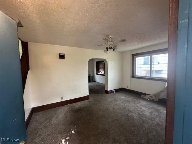 spare room with baseboards, a textured ceiling, arched walkways, and a ceiling fan