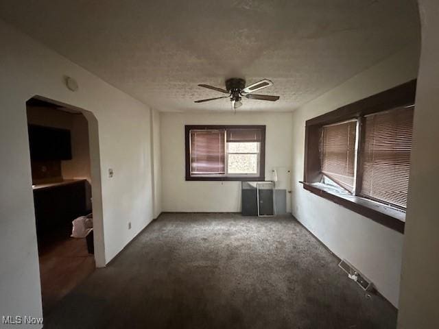 carpeted empty room with arched walkways, ceiling fan, and a textured ceiling