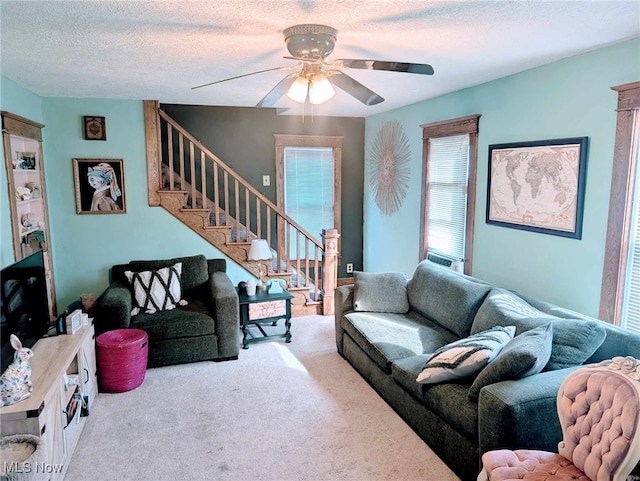 living area featuring stairs, ceiling fan, a textured ceiling, and carpet flooring