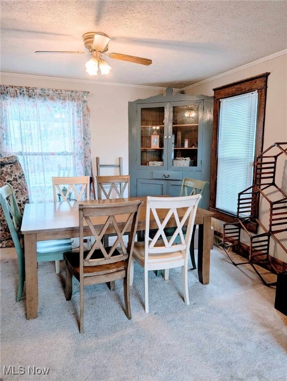 dining area with a ceiling fan, ornamental molding, a textured ceiling, and light colored carpet