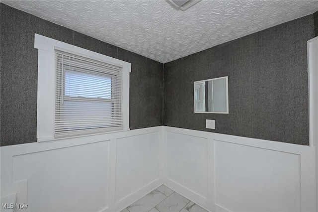 spare room with marble finish floor, a wainscoted wall, and a textured ceiling