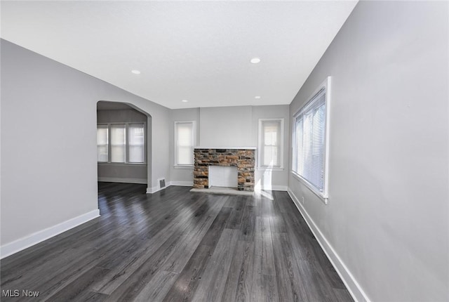 unfurnished living room with arched walkways, recessed lighting, a fireplace, baseboards, and dark wood-style floors