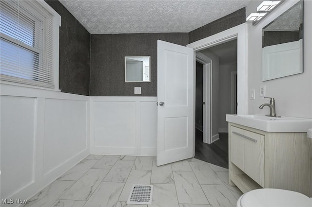 bathroom with a textured ceiling, visible vents, vanity, marble finish floor, and wainscoting