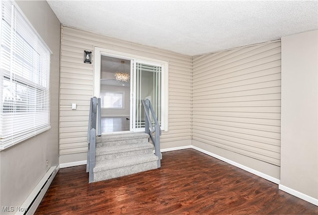 interior space with a textured ceiling, baseboard heating, wood finished floors, and baseboards