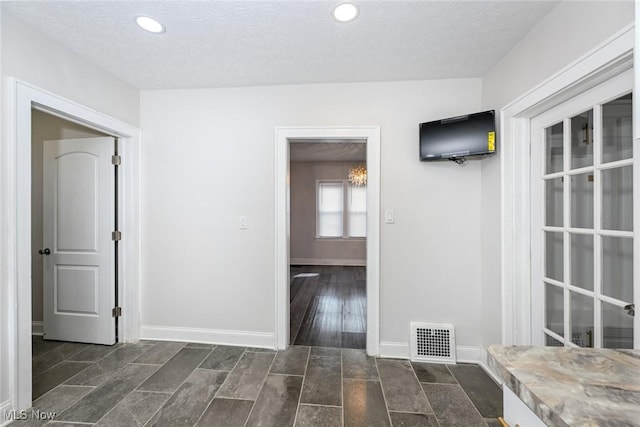 interior space featuring dark wood-style flooring, visible vents, a textured ceiling, and baseboards