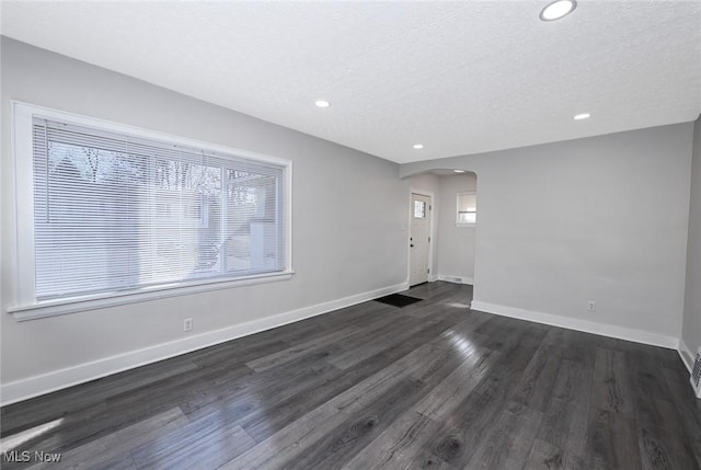 interior space with arched walkways, a textured ceiling, recessed lighting, baseboards, and dark wood finished floors