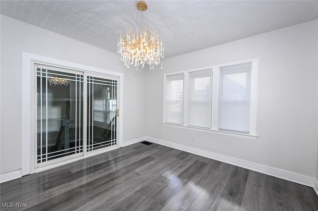 spare room featuring a notable chandelier, dark wood finished floors, a textured ceiling, and baseboards