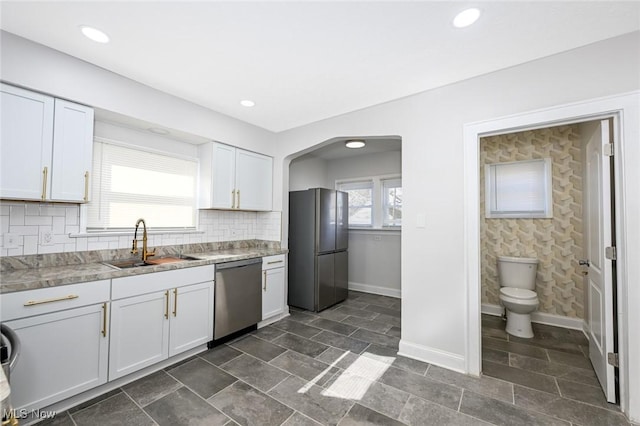 kitchen featuring decorative backsplash, stainless steel dishwasher, freestanding refrigerator, white cabinetry, and a sink