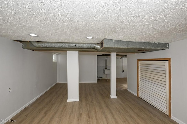 finished basement featuring a sink, a textured ceiling, baseboards, and wood finished floors