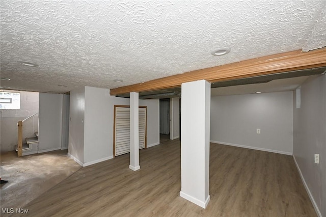 finished below grade area featuring a textured ceiling, wood finished floors, stairs, and baseboards