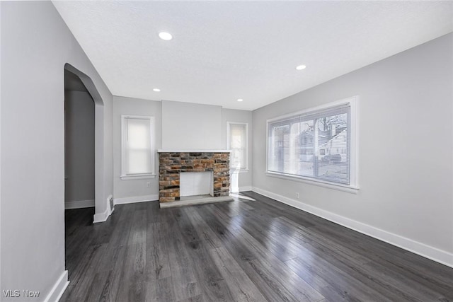 unfurnished living room with baseboards, arched walkways, a fireplace with raised hearth, and dark wood-type flooring