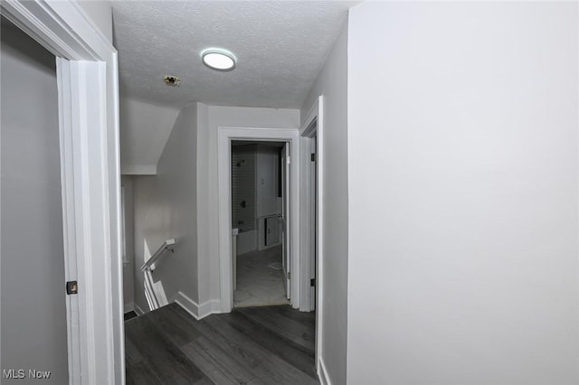 corridor featuring a textured ceiling, baseboards, dark wood-style flooring, and an upstairs landing