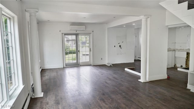 empty room featuring a baseboard radiator, a wall unit AC, ornate columns, and wood finished floors